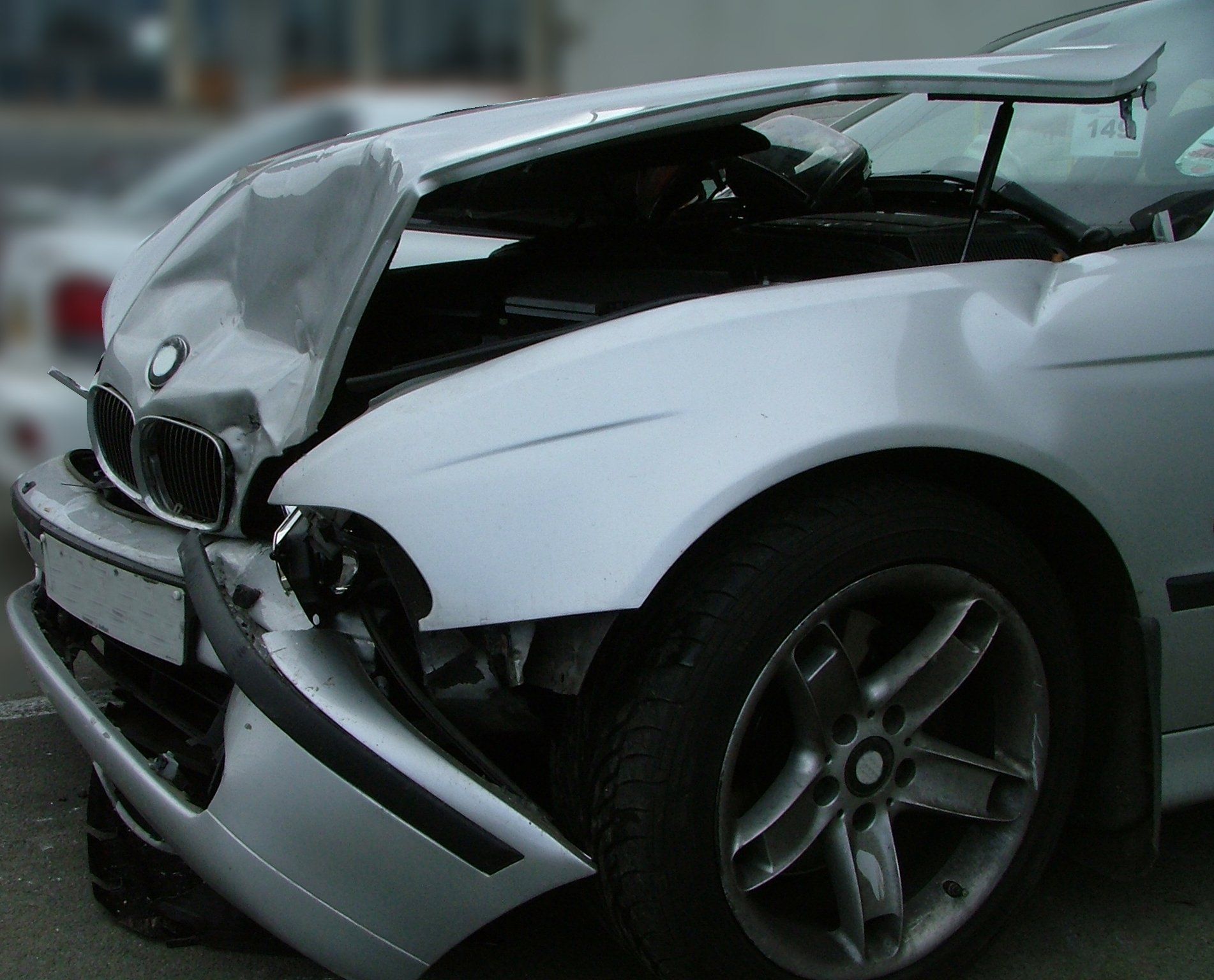 Damaged silver BMW car after a front-end collision. Hood crumpled, bumper detached.