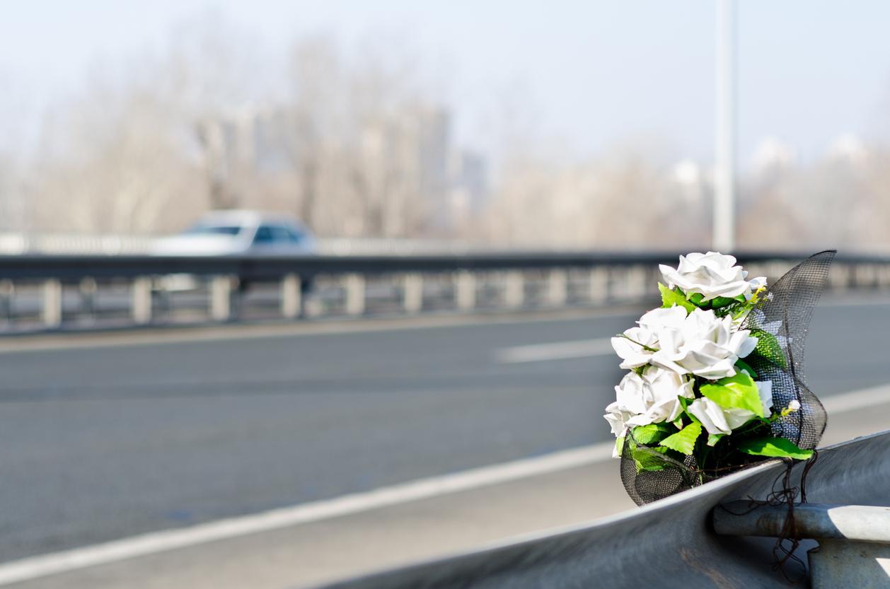 White flowers on highway guardrail; car in background.
