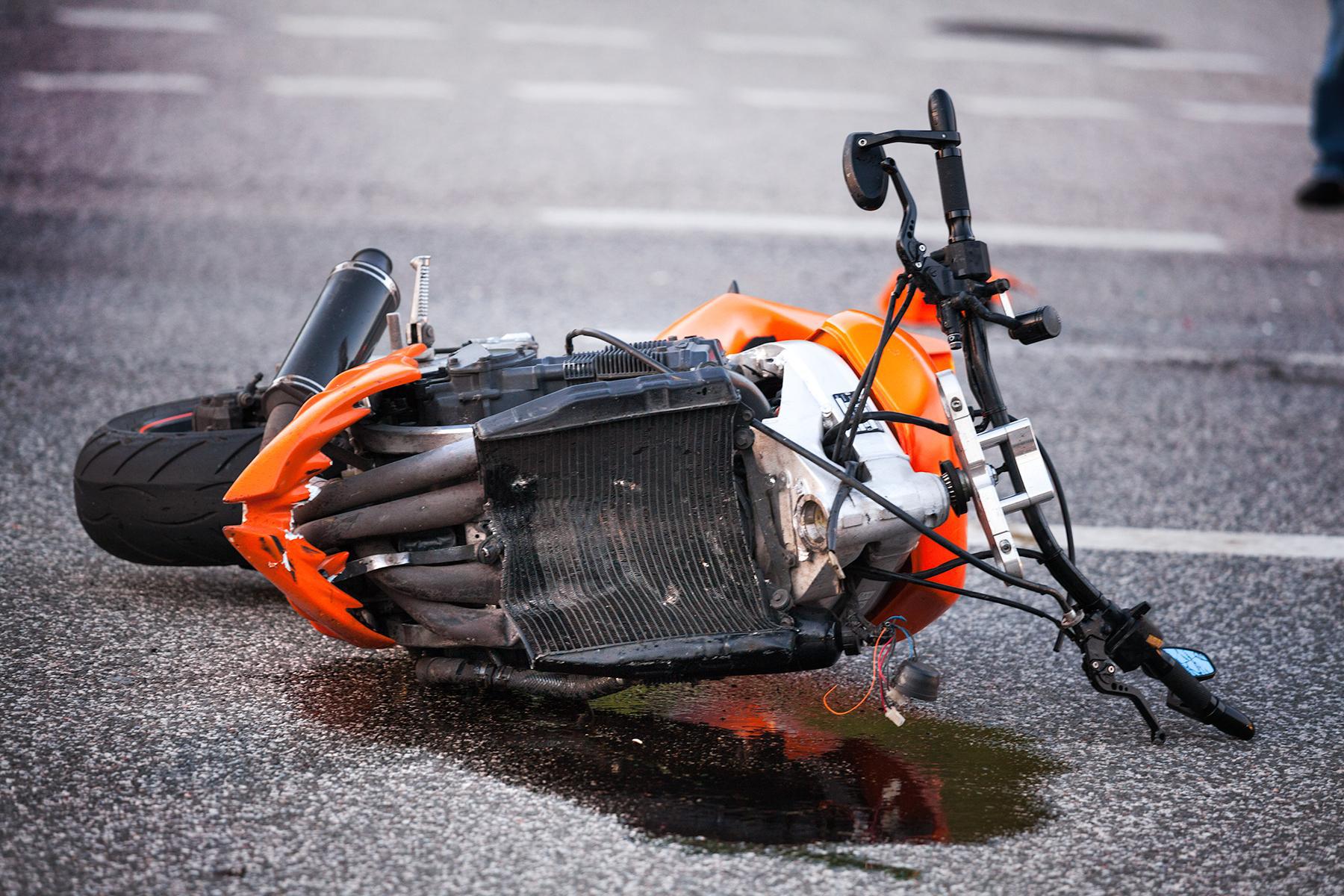 Orange motorcycle lying on its side on a wet road after an accident.