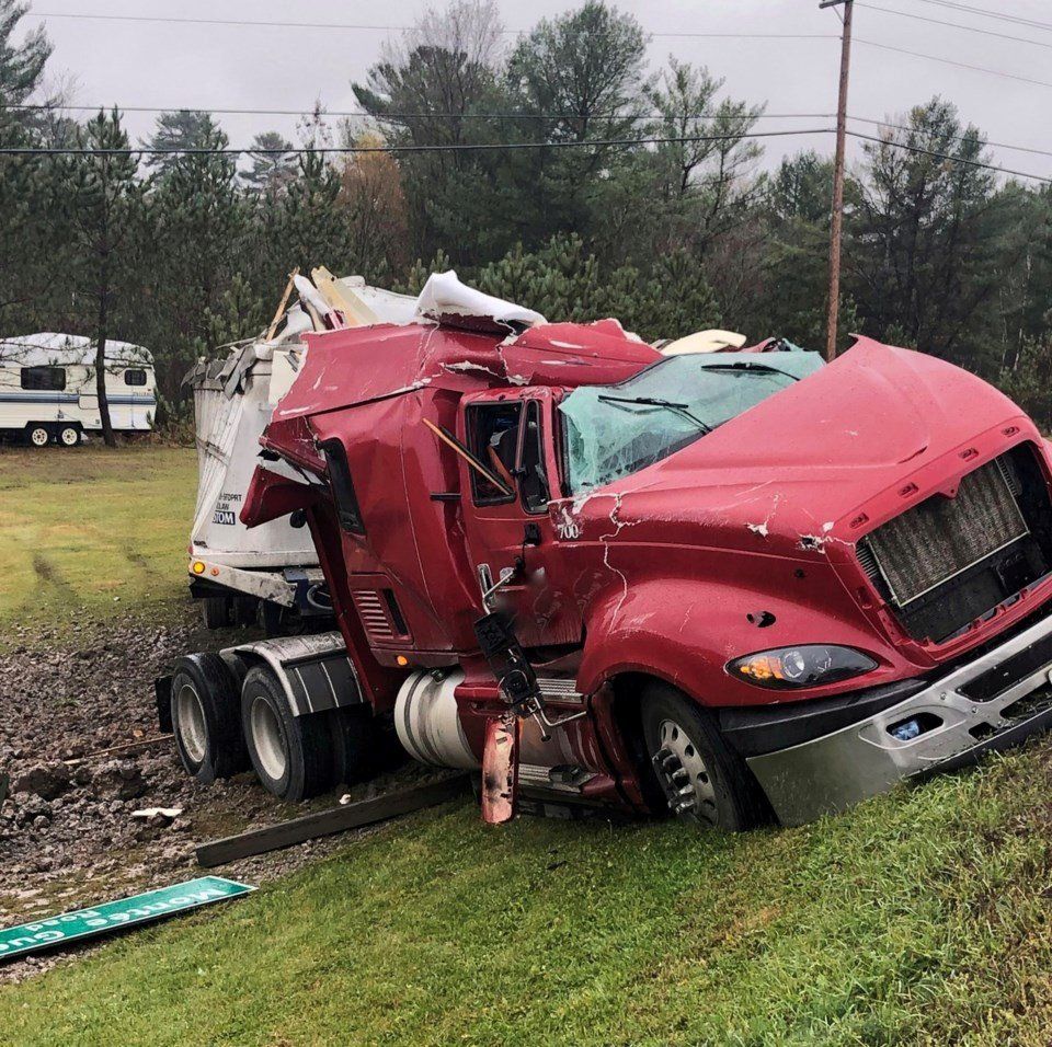 Red semi-truck crashed off the road into a grassy area with extensive damage.