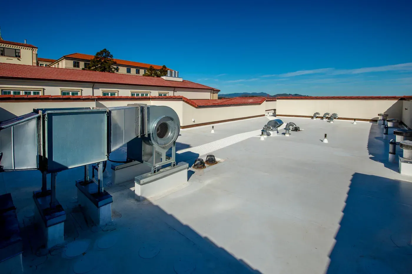 The roof of a Bakersfield, CA building with a white roof and a fan on it.
