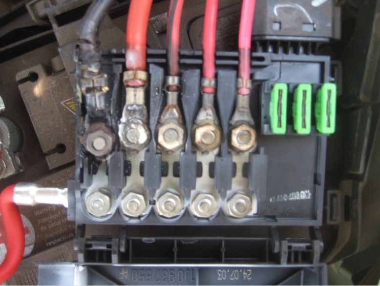 Black car fuse box with red wires and green fuses. Some wires show signs of heat damage.