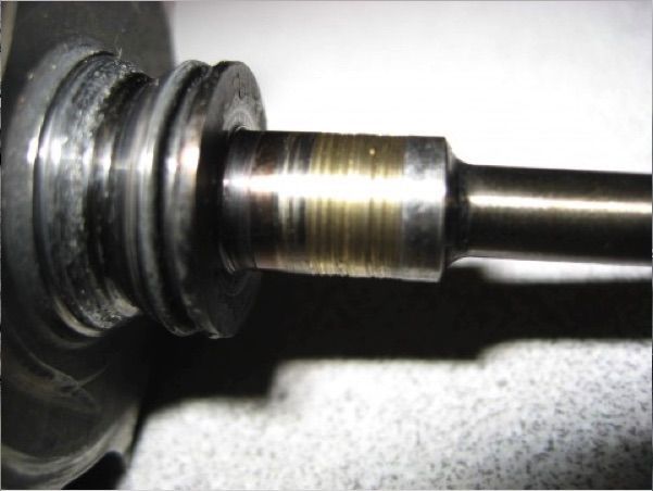Close-up of a worn metal shaft with grooves and wear marks, likely part of a machine component.