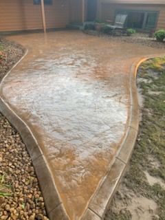 Wet concrete walkway leading to a house entrance, bordered by landscaping rocks and grass.