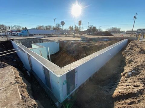 Concrete foundation pit at a construction site with dirt walls and bright sunlight.