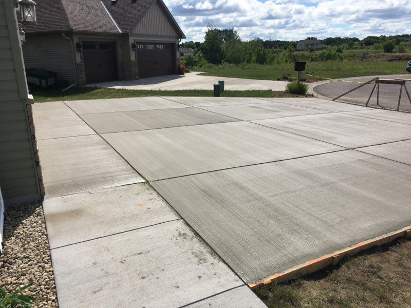 New concrete driveway beside a house, with garage and grassy yard in the background.