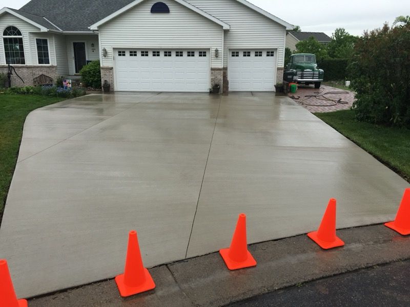 Freshly poured concrete driveway in front of a suburban garage, marked with orange safety cones