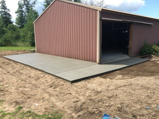Brown metal shed with a large concrete pad and open doorway on a dirt lot