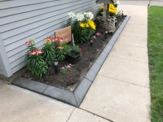 Small flower bed with colorful plants and flowers beside a house along a concrete sidewalk