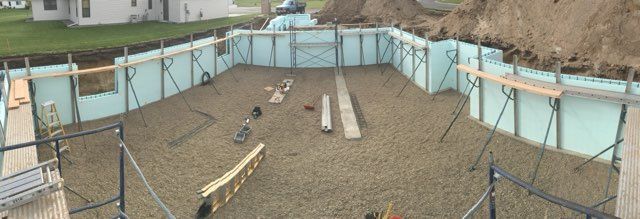 Construction site with gravel floor, pale blue barriers, and wooden planks laid across the ground.