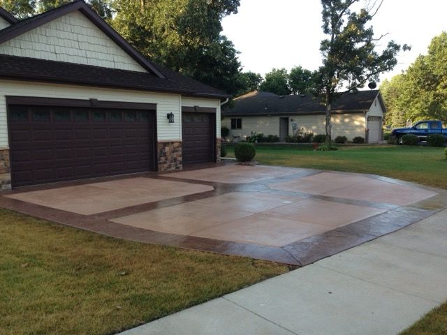 Suburban driveway with a dark garage door, fresh concrete pad, and a house in the background
