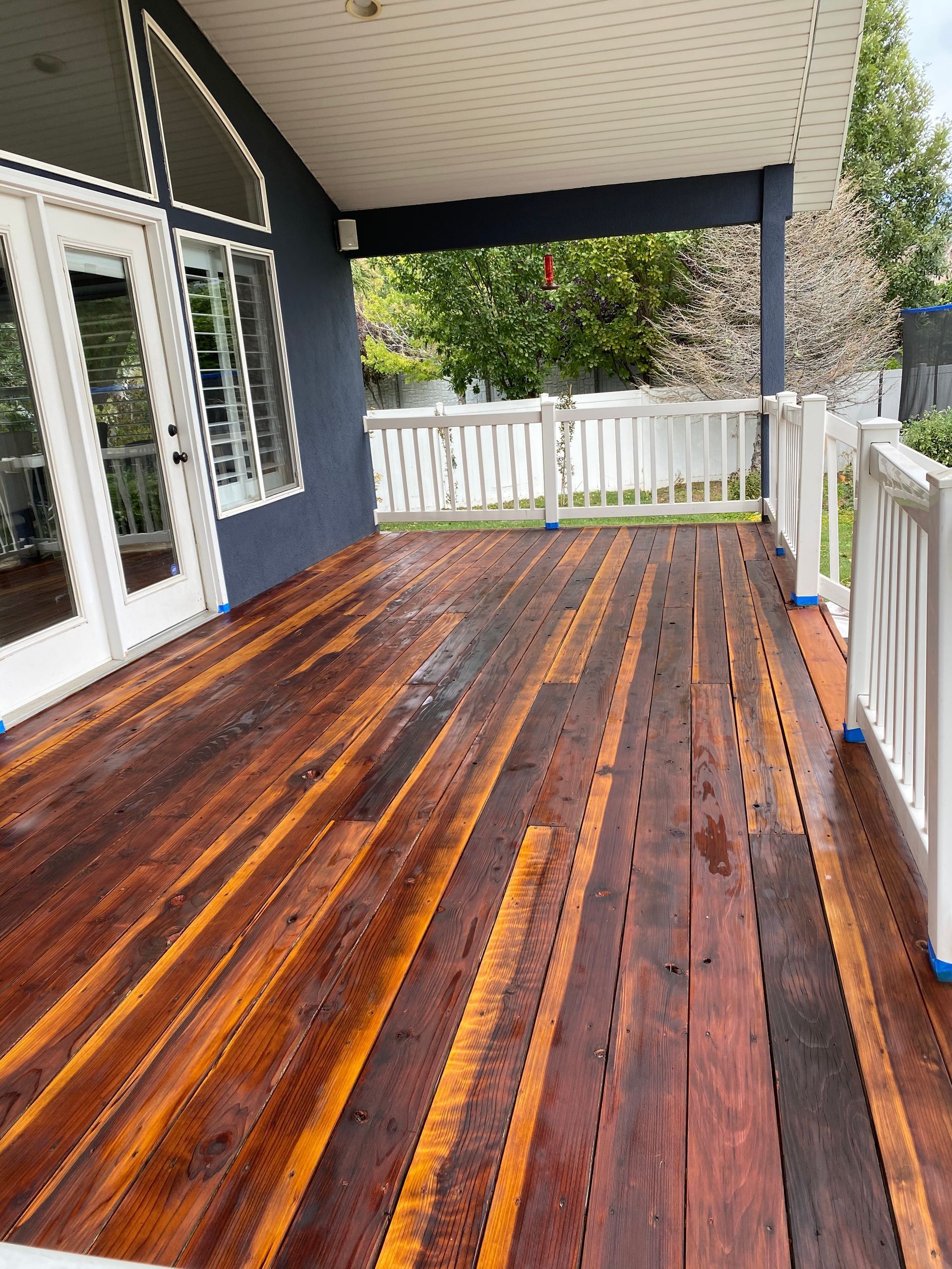 a large wooden deck with a white railing and a blue building in the background .