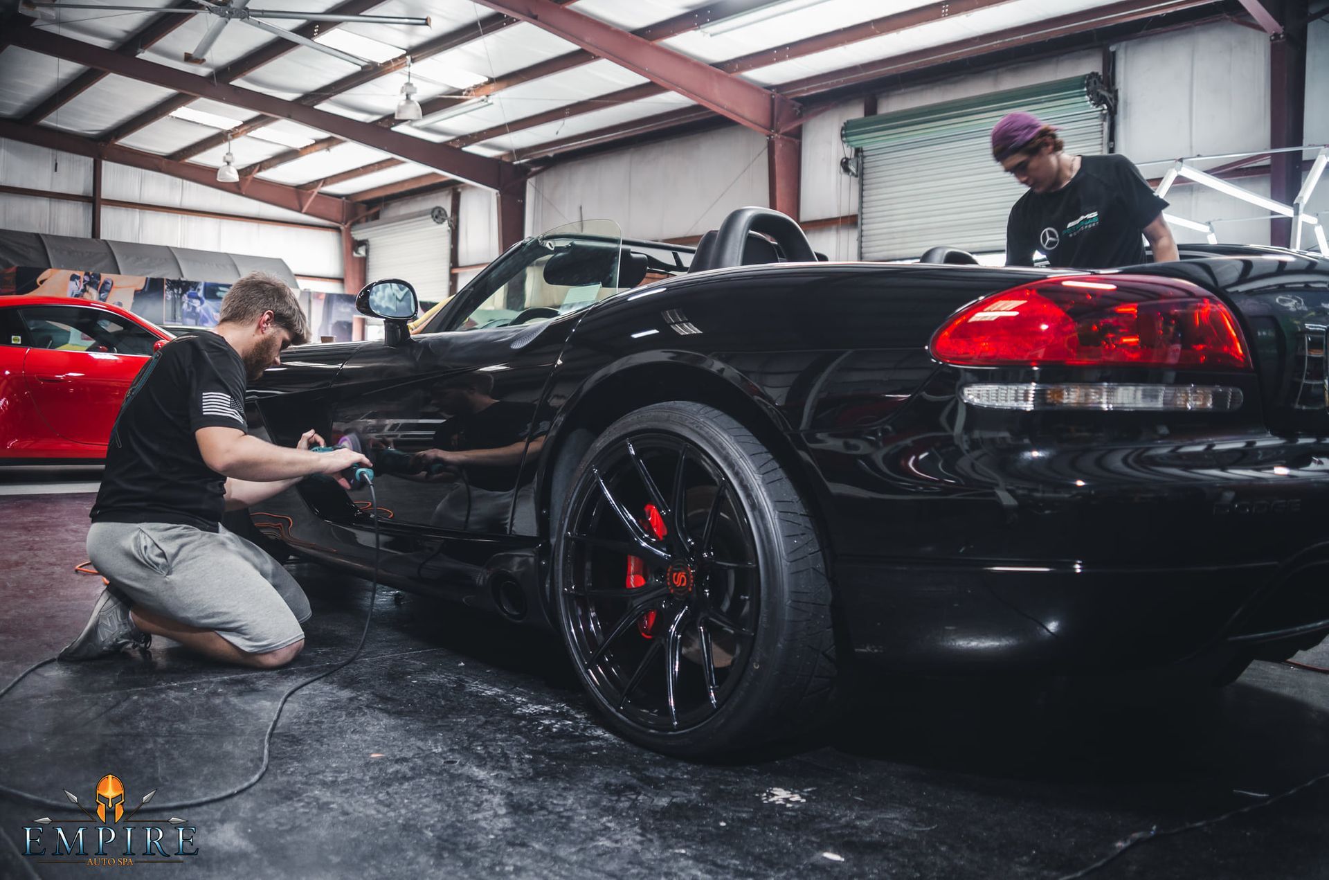 Two men are working on a black car in a garage.