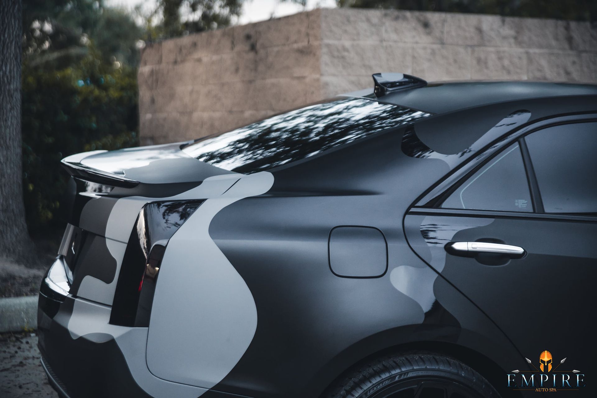 A black car with a camouflage design on the side is parked in front of a brick wall.