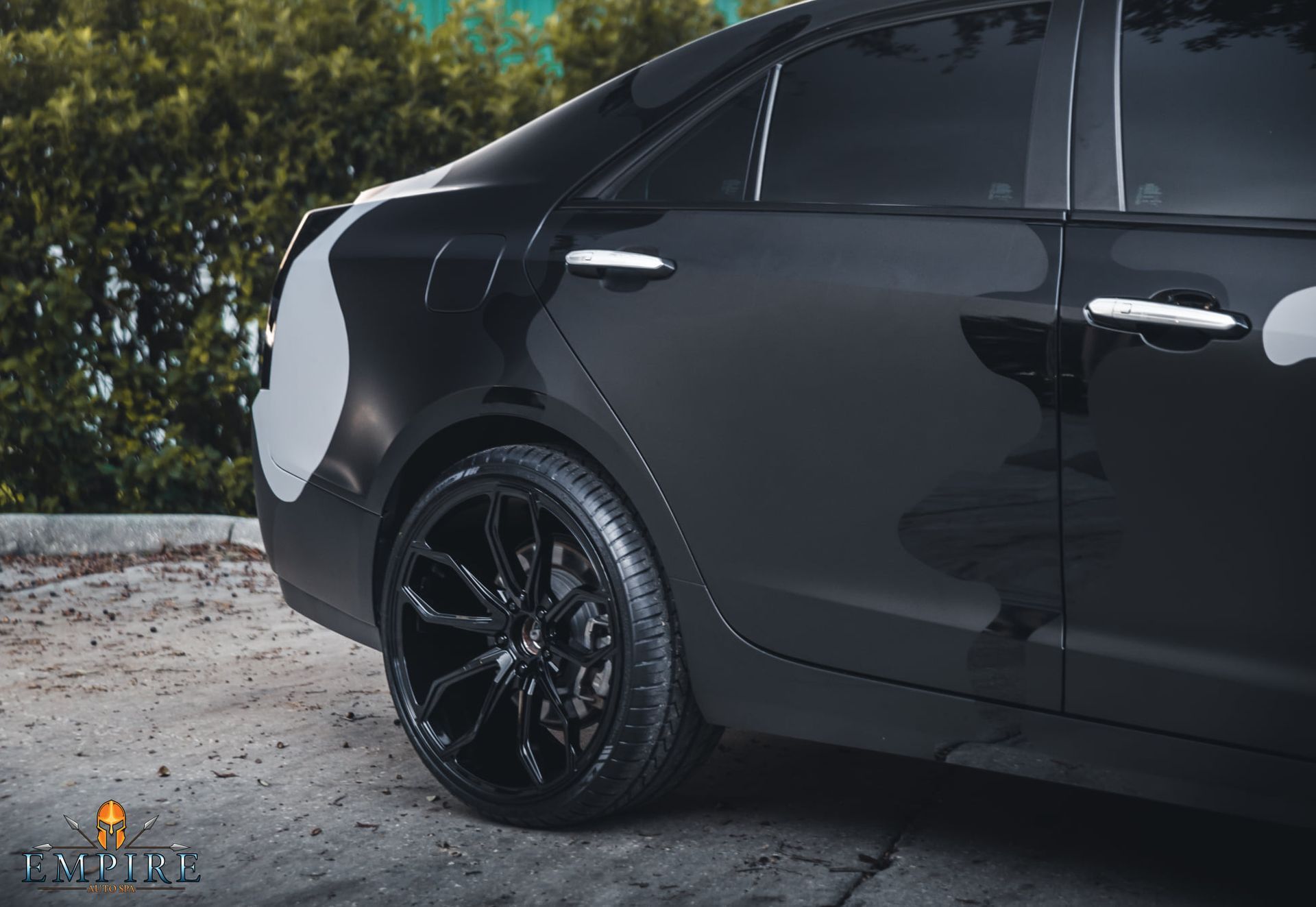 A black car is parked in a parking lot with trees in the background.
