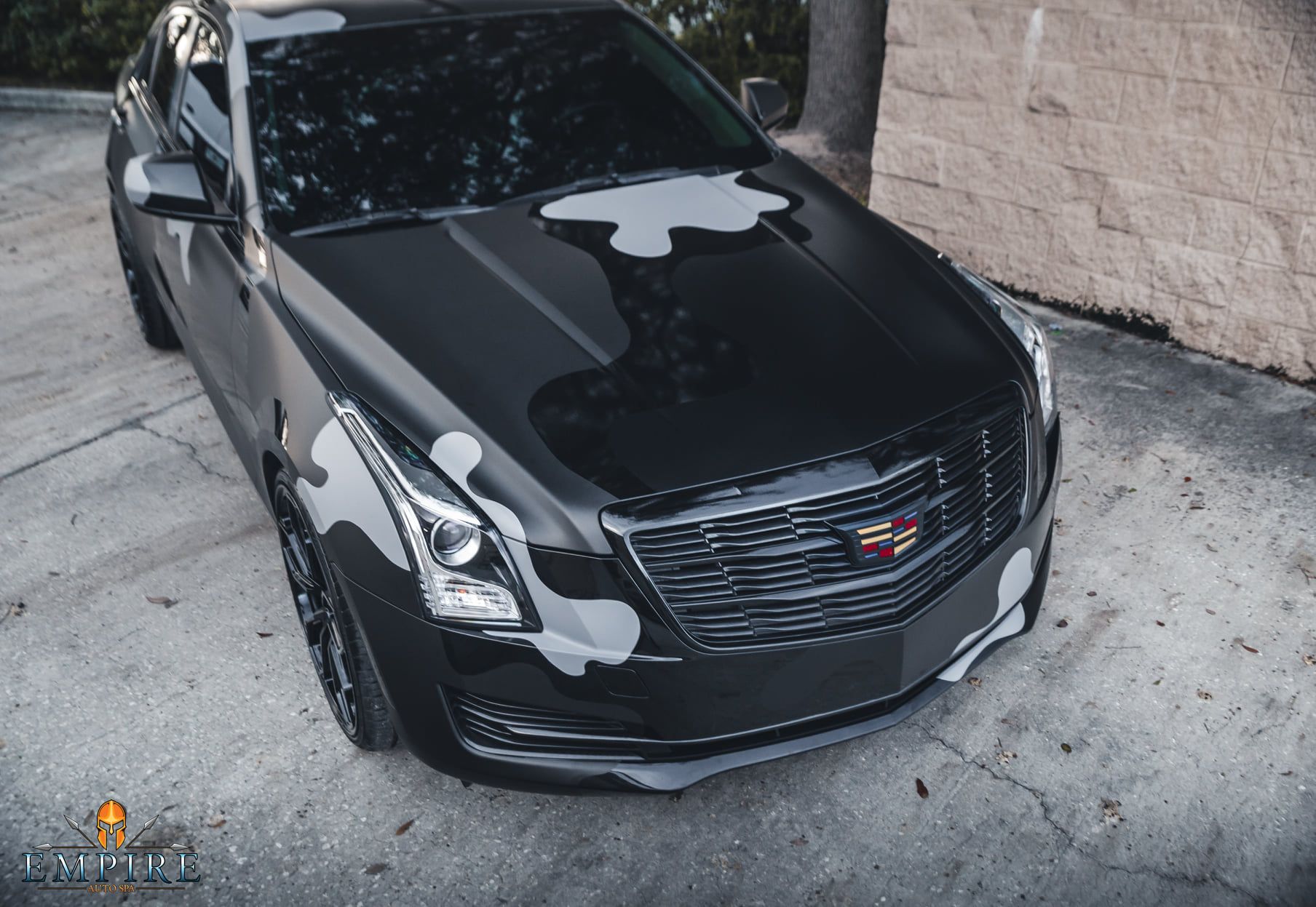 A black cadillac is parked in front of a brick wall.