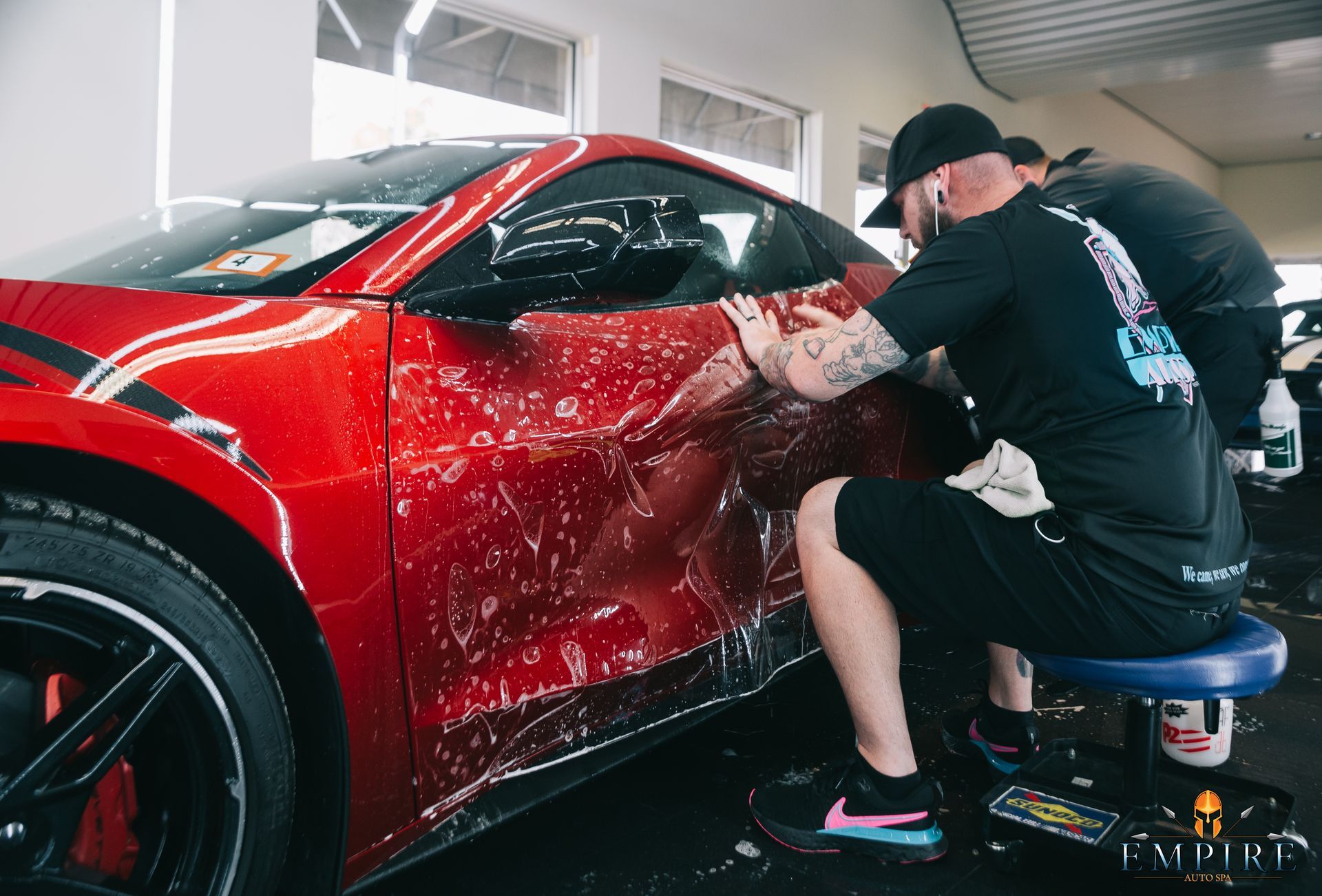 A man is sitting on a stool wrapping a red sports car.