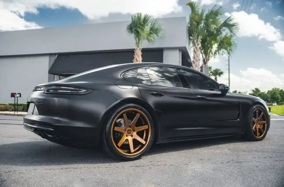 A black car with gold wheels is parked in front of a building.