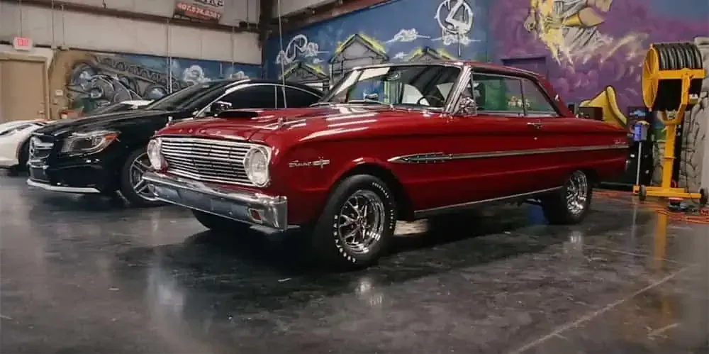 A red car is parked next to a black car in a garage.