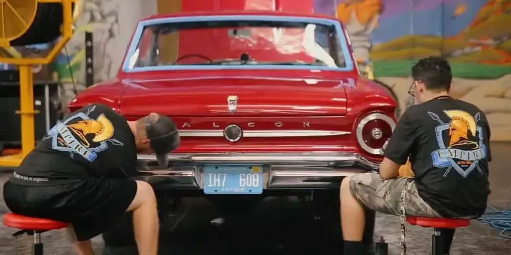 Two men are working on a red car in a garage.