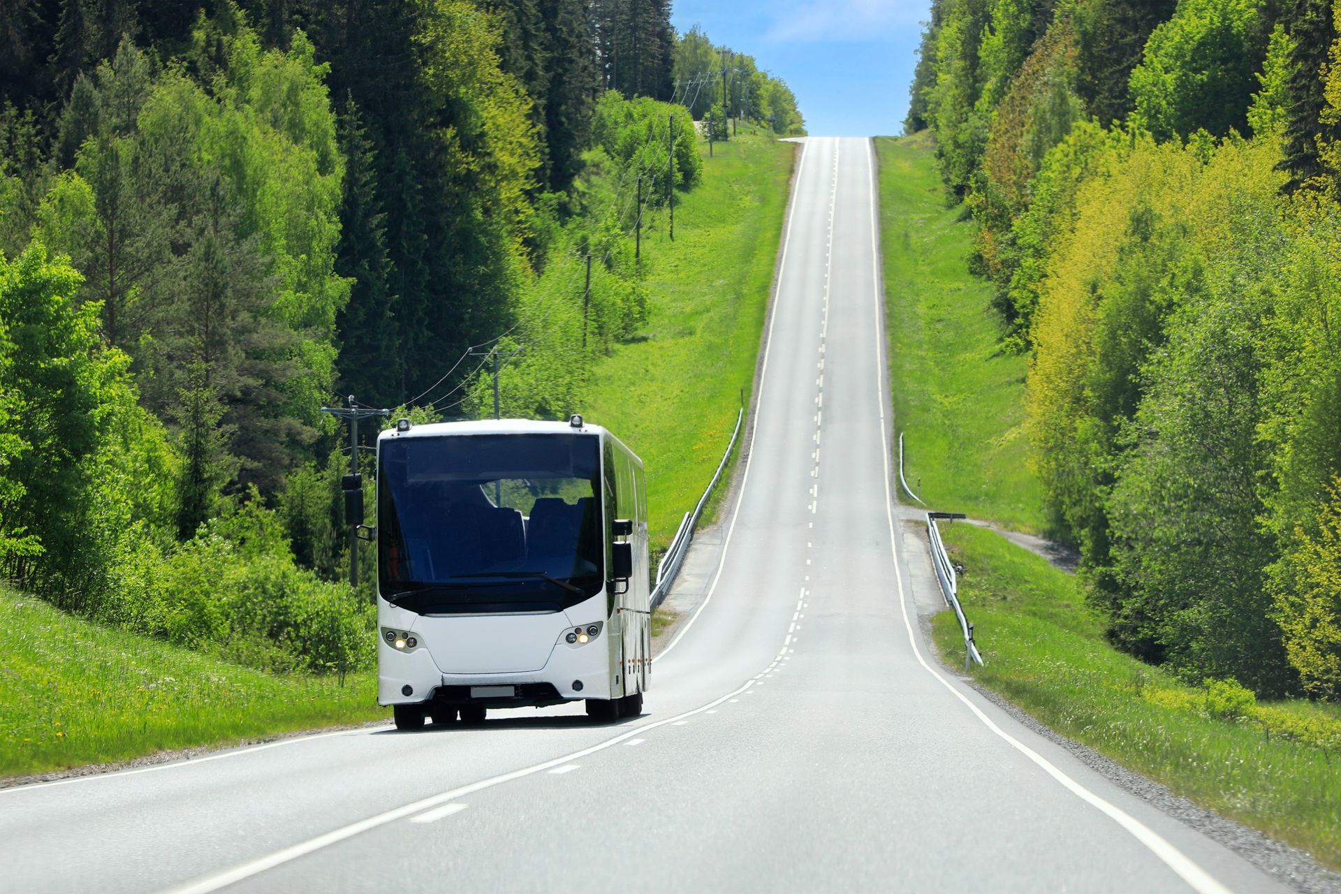 White bus traveling on a highway through scenic countryside under a clear blue sky