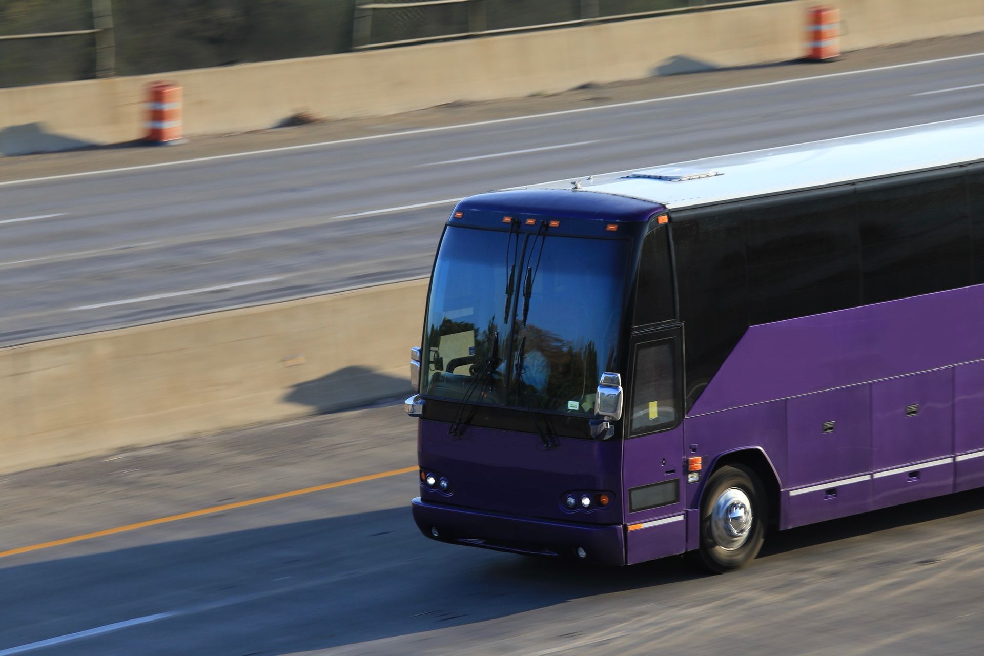 A purple private charter bus drives on the highway past cones and barriers.