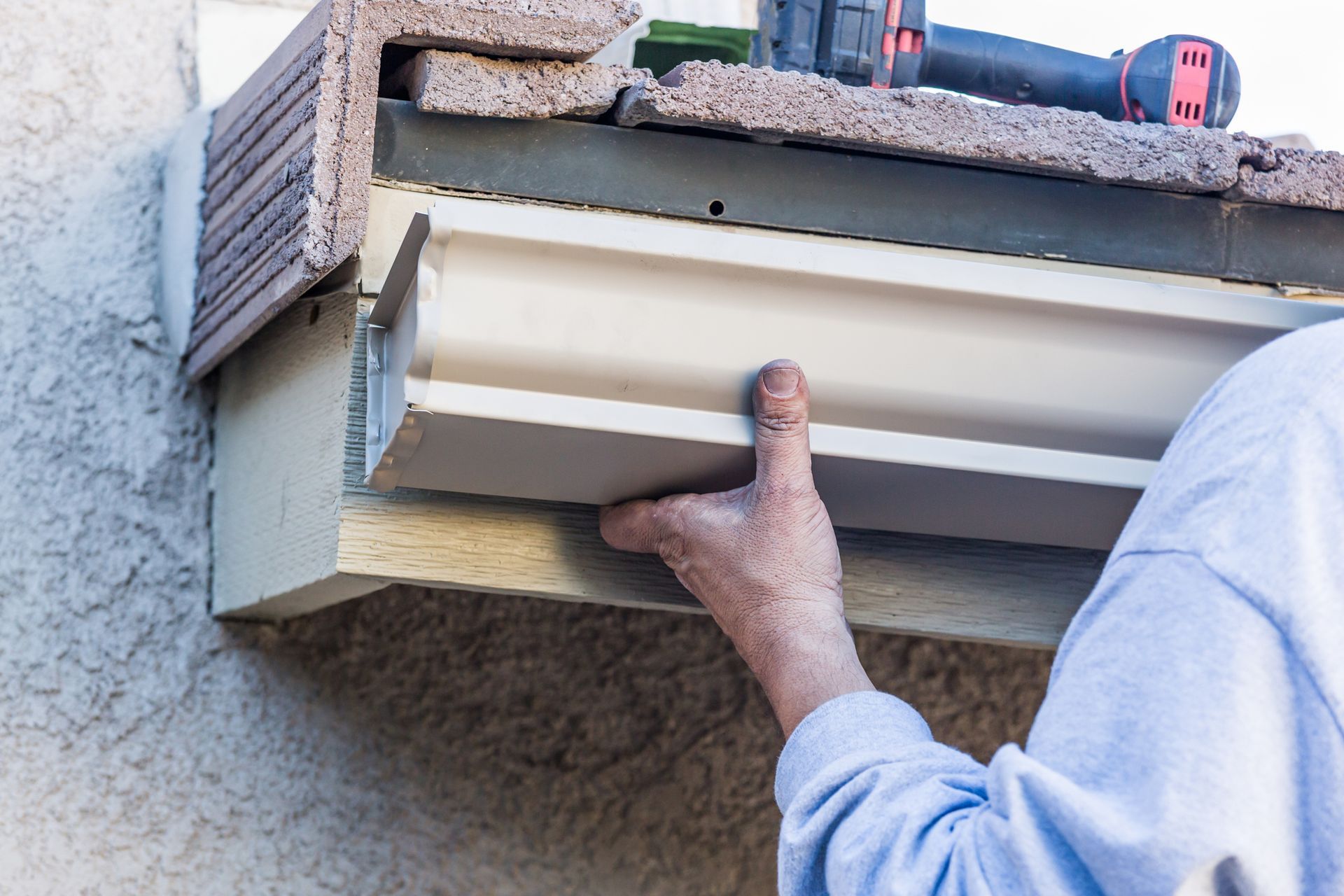 A man is installing a gutter on the side of a building.