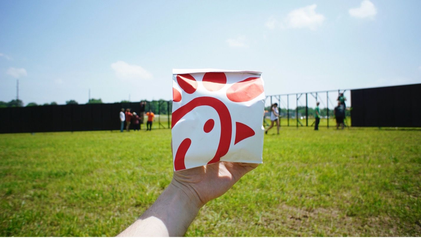 A person is holding a chick fil a cup in front of a field
