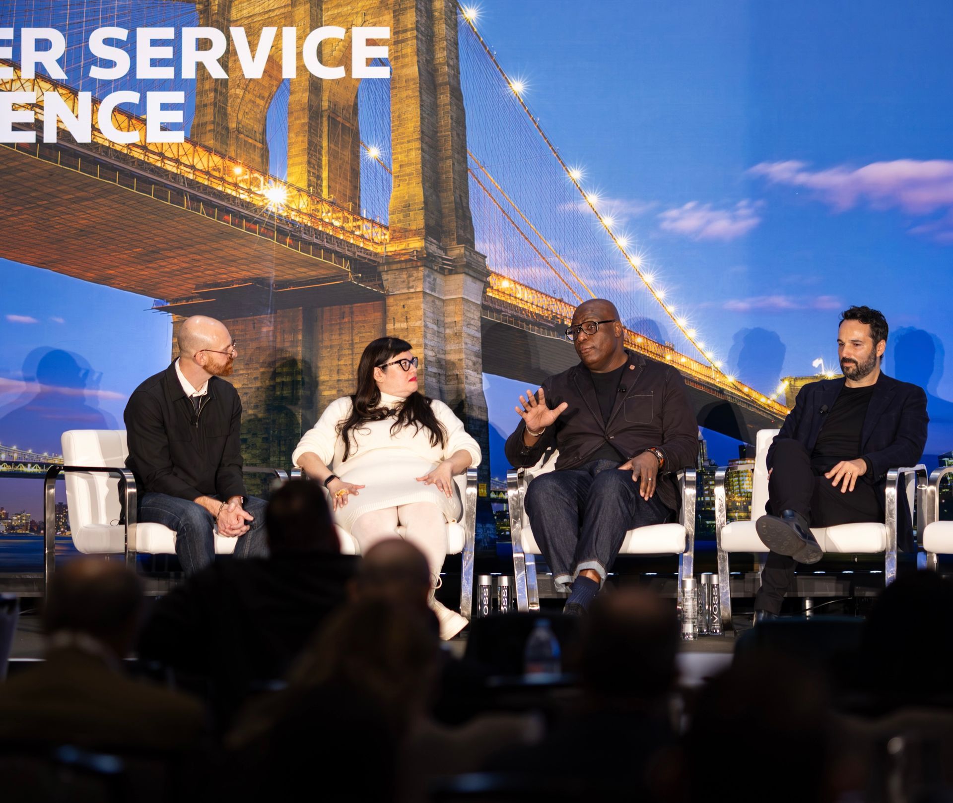 Panel discussion with four people on stage, backdrop of the Brooklyn Bridge.