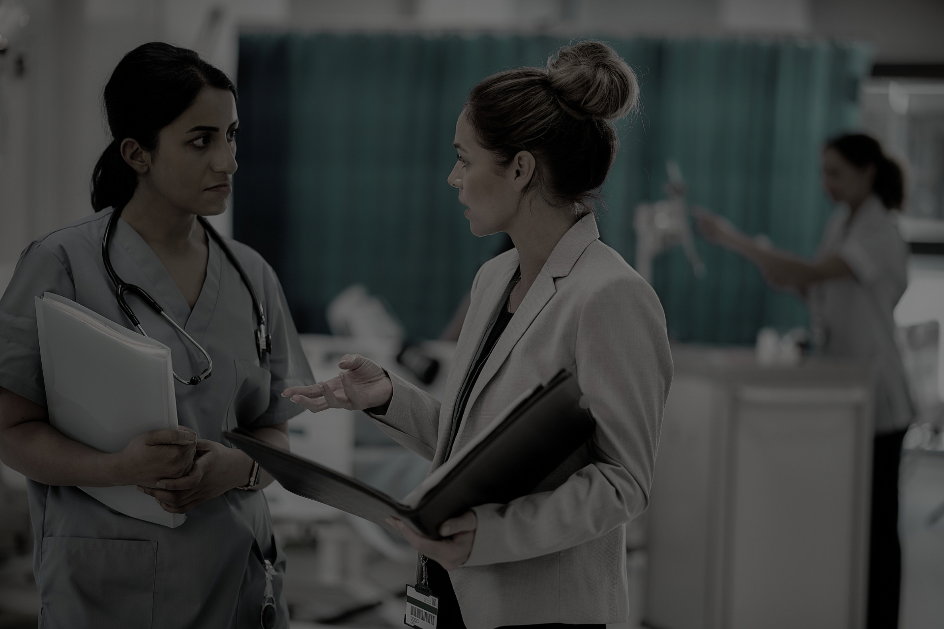 Two clinicians talking in a hospital corridor, holding charts and a tablet.