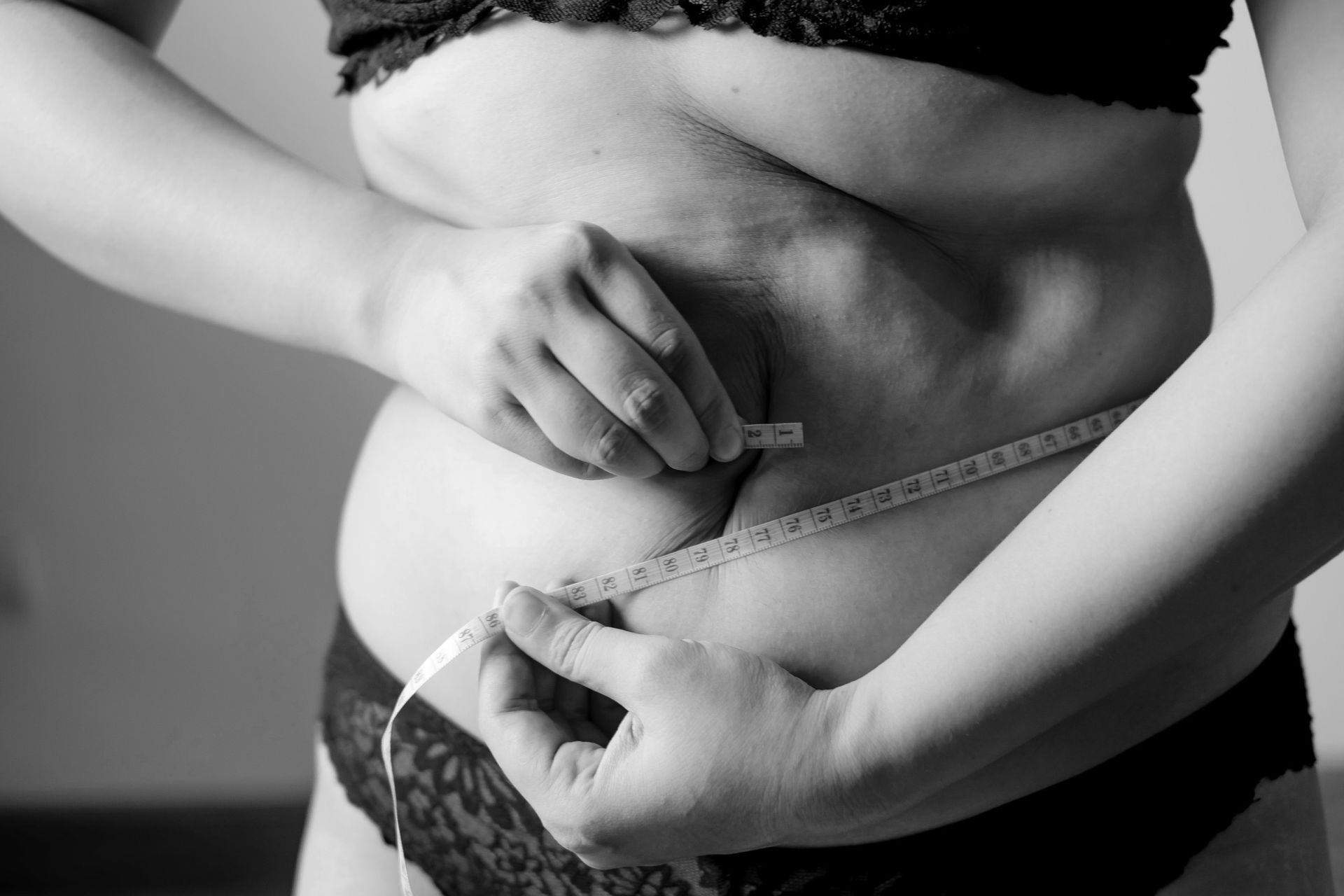 Person measuring waist with a tape measure in black underwear, black-and-white image