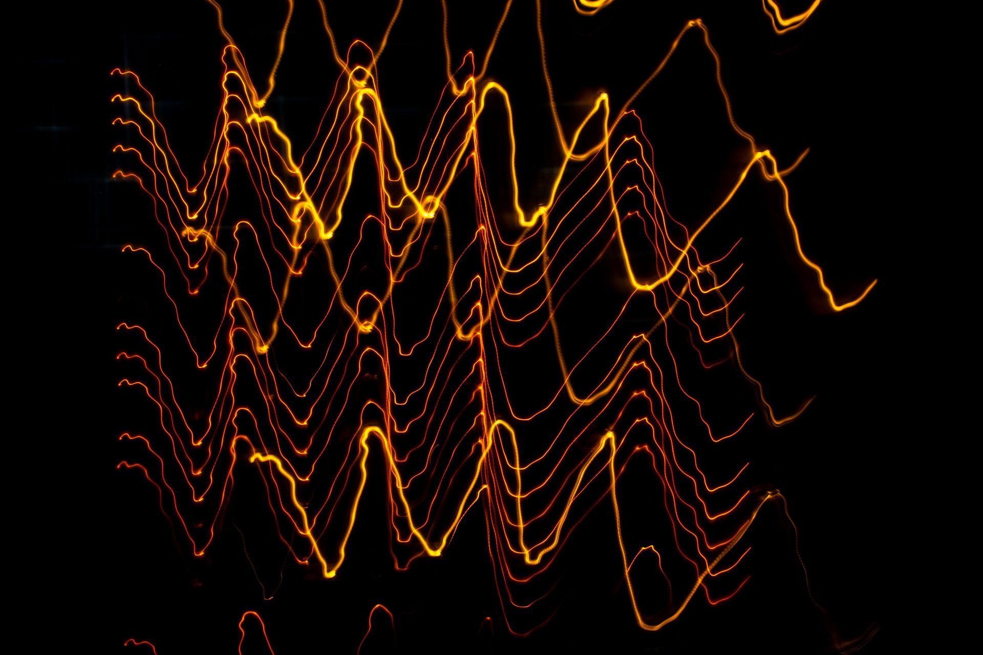 Abstract orange-yellow light trails on a black background, forming wavy vertical lines