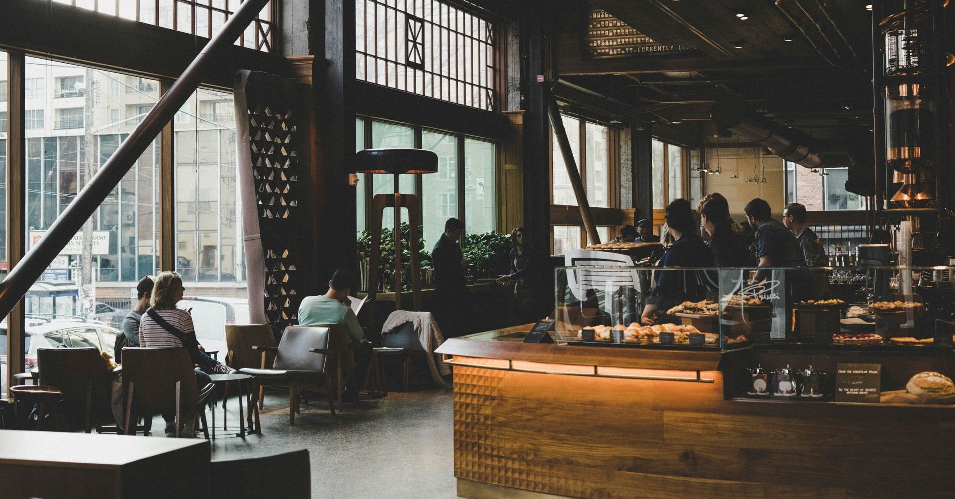 Industrial-style café with large windows, people seated at tables, and a bright wooden counter