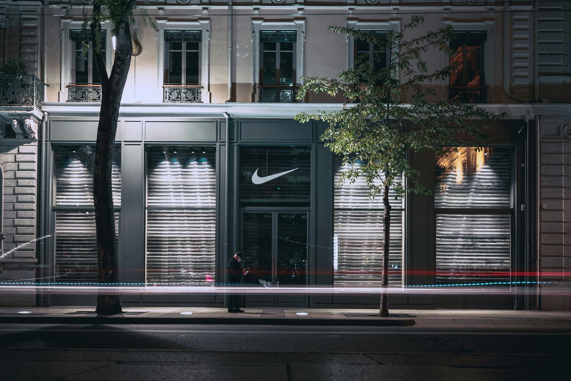A man is walking in front of a nike store at night.