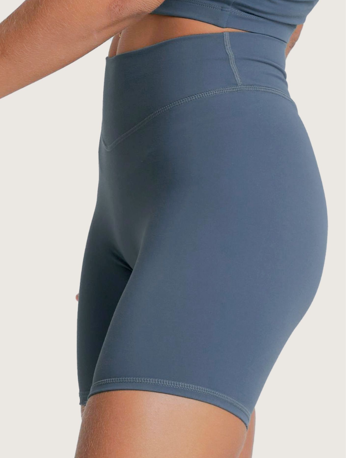Person wearing blue athletic top and shorts, standing with hands on hips against a white background