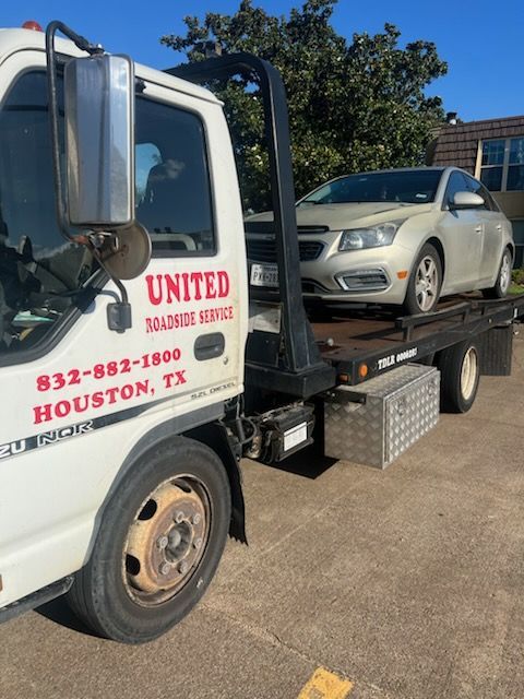 Tow truck loading a silver car on a flatbed in a sunny parking lot