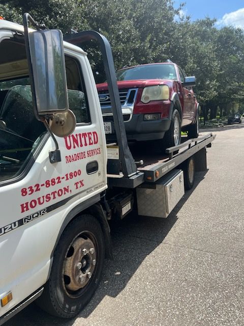 Tow truck hauling a red SUV on a flatbed trailer on a sunny road