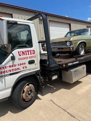 Tow truck hauling a vintage green car outside a garage in Houston, TX