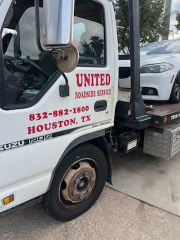 Tow truck with United Roadside Service logo loading a white car in Houston, Texas.