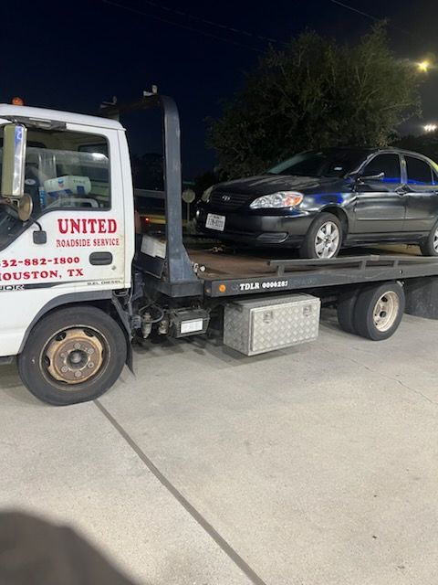 Tow truck hauling a black sedan at night on a street or driveway.