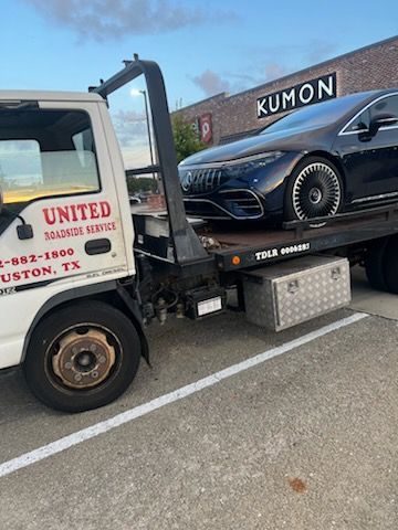 Tow truck hauling a black Mercedes SUV in a parking lot near a Kumon building
