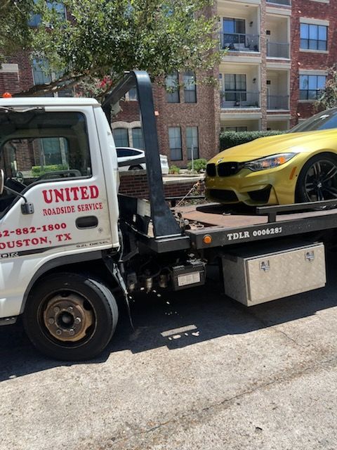 Tow truck loading a yellow sedan on a city street beside an apartment building