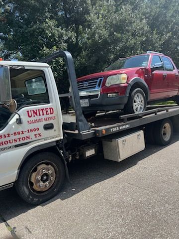 Tow truck hauling a red SUV on a flatbed on a tree-lined road.