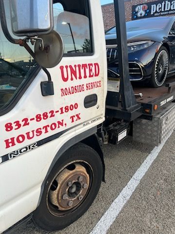 Tow truck with “United Roadside Service” text hauling a car on a trailer by the roadside