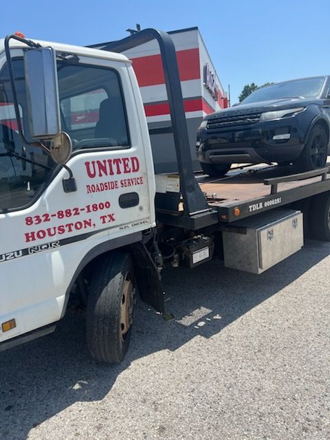 Tow truck hauling a black SUV on a flatbed in a parking lot under bright sun