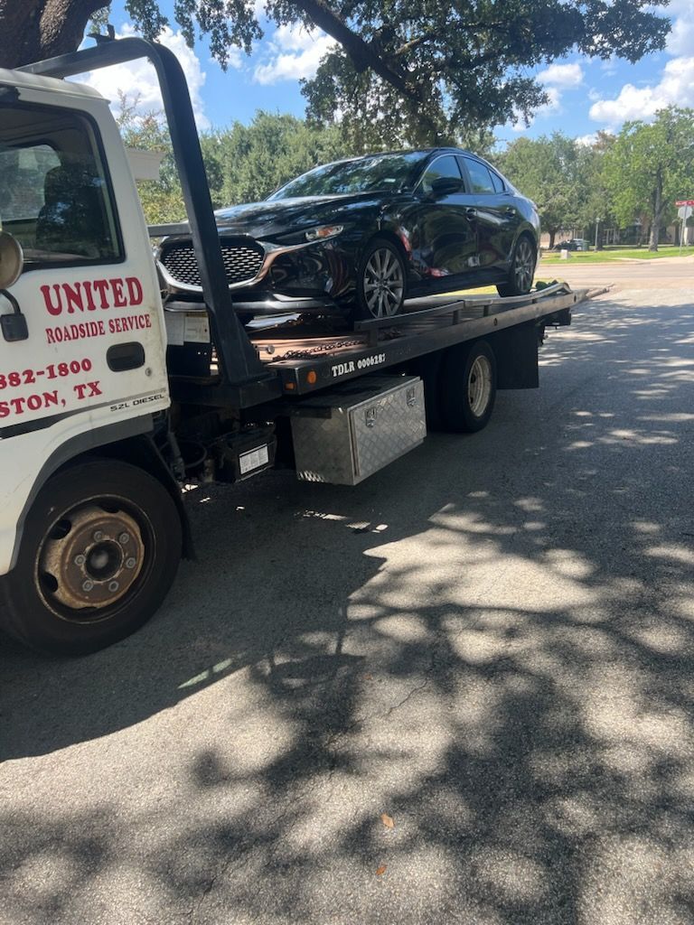 Black SUV on a tow truck parked on a tree-lined street in daylight