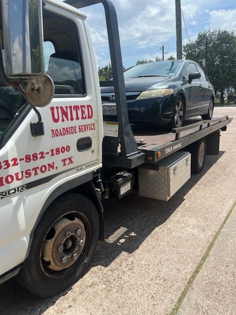 Tow truck hauling a black SUV on a flatbed along a sunny roadside.
