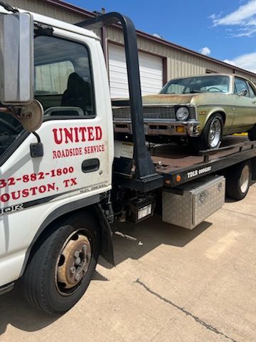 White tow truck hauling a vintage green car on a flatbed in an industrial lot