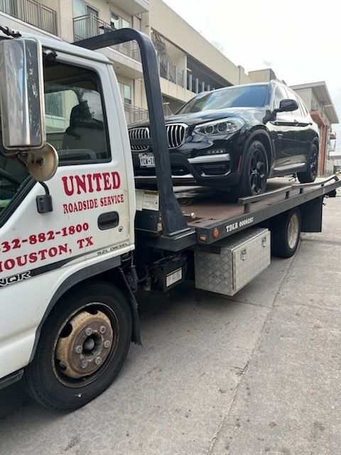 Tow truck hauling a black SUV on a city street, with United Towing Service on the cab.