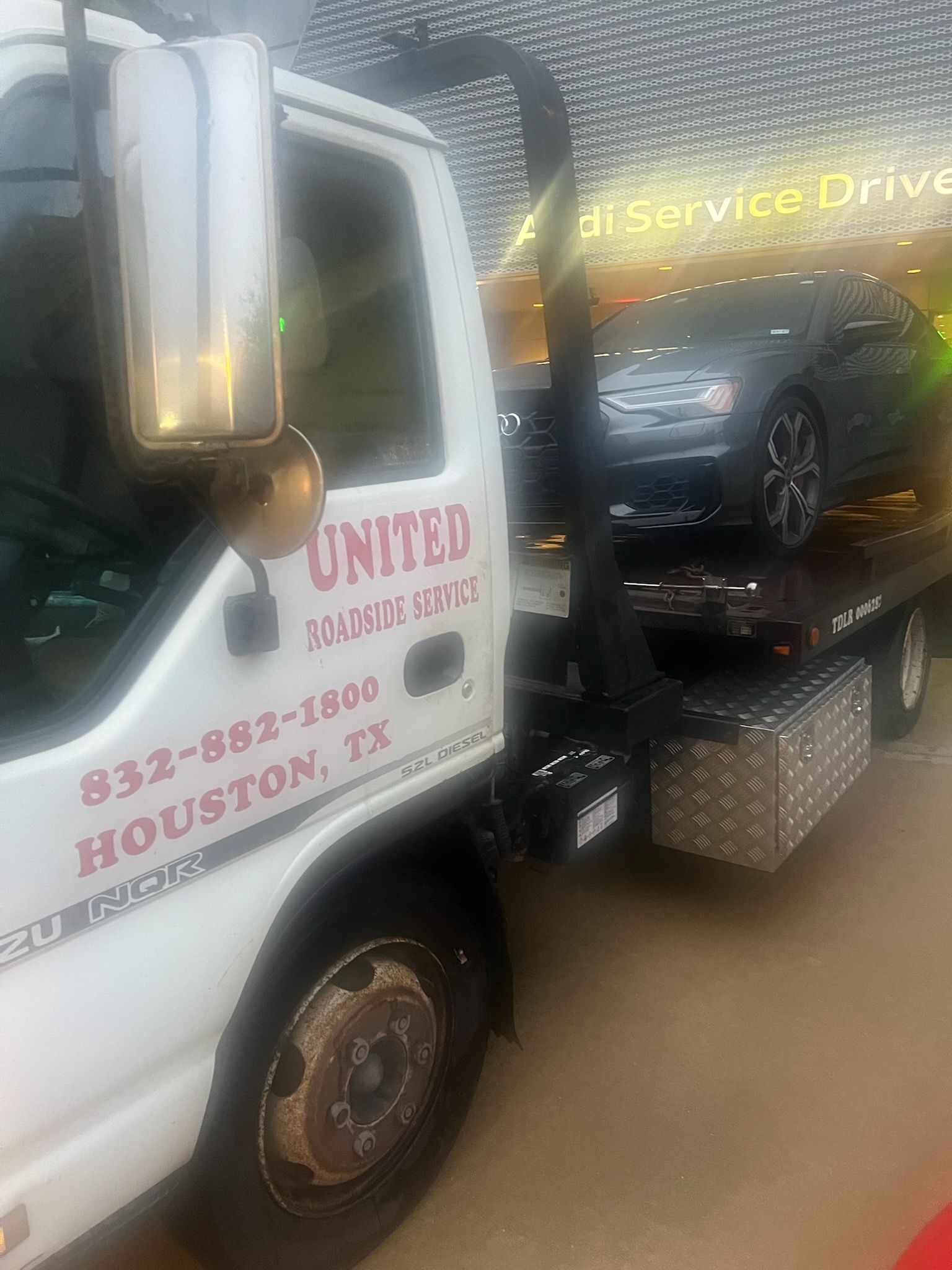 White tow truck with “United Towing” text hauling a black car on a wet road in the rain